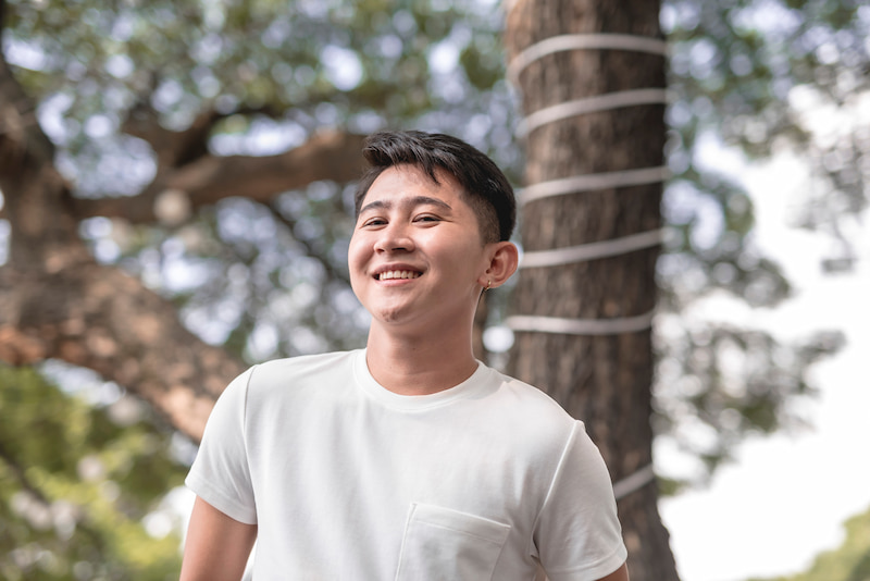 :A man with an undercut standing in front of a tree and smiling.